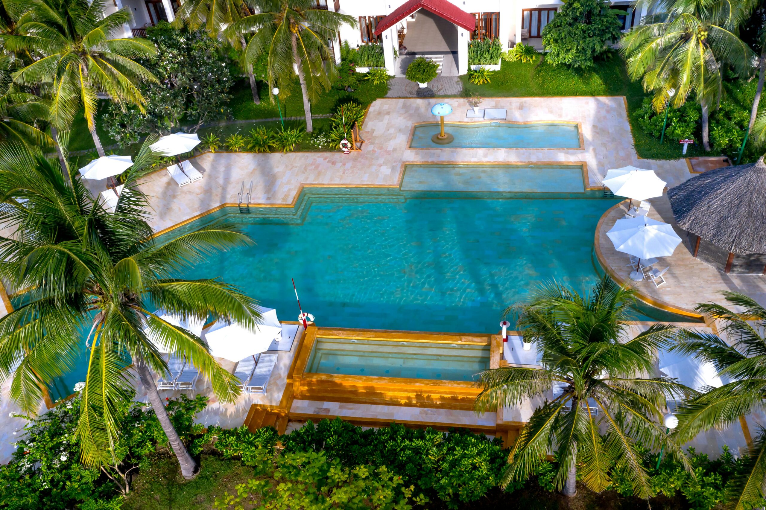 Aerial view of a luxurious tropical resort with swimming pool and palm trees.