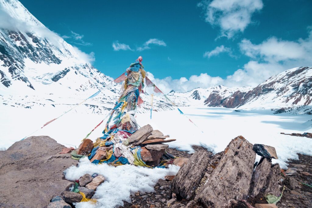 pexels-photo-15620431-15620431 Scenic snowy mountain landscape in Manang, Nepal with colorful prayer flags against a clear sky.