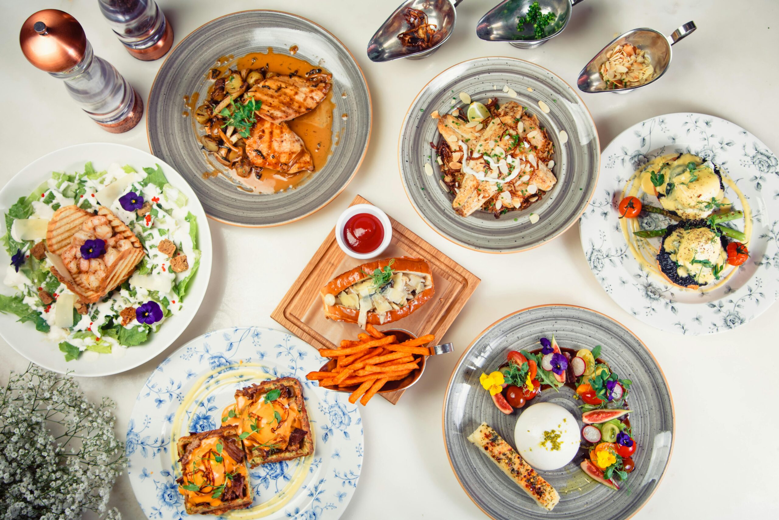A top view of diverse gourmet dishes arranged on a white surface, showcasing culinary variety and elegance.